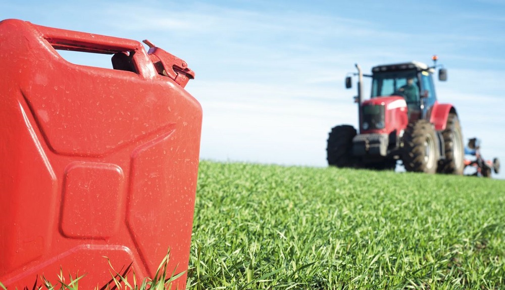 A red fuel can in a field with a red tractor in the distance.